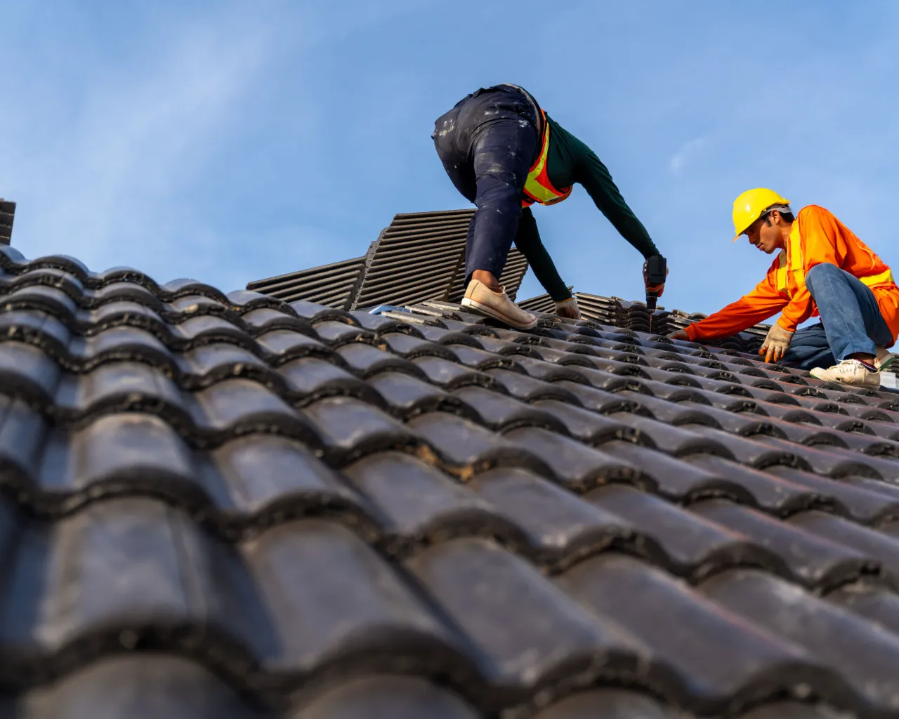 Dois trabalhadores fixando telhas em telhado residencial durante reparo
